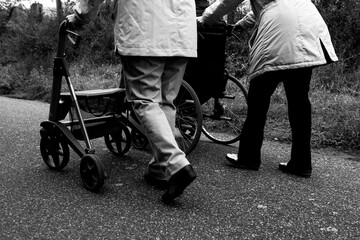 Obraz premium Elderly friends taking a walk in the park during cold weather with help of wheelchair and walker enjoying and having fun