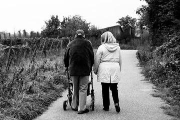 Elderly people taking a walk with help of walker with friends on a cold day through the park