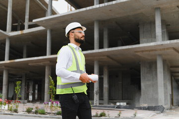 Engineer supervising building construction site holding blueprints