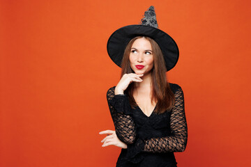 Young pensive woman wears black hat dress witch costume put hand prop up on chin, lost in thought...