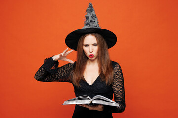 Young wicked woman she wears black hat dress witch costume hold and magic book casting dark spell...