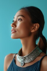 Young asian female in profile with silver necklace against blue background
