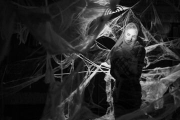 Creepy man with scary Halloween zombie makeup trapped spider webs, trying to scare. Dead guy in cob web on dark background.