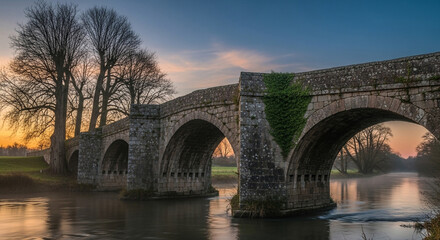 Fototapeta premium Scenic stone bridge over the river avon in the cotswolds at sunrise, with mist rising from the water and trees silhouetted against the sky, england, uk