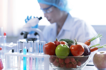 Food scientist in a laboratory examines a sample under a microscope, researching nutrition and food safety. Fresh vegetables on the table represent healthy organic food testing and quality control.