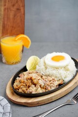 Delicious plate of crispy pork sisig with steamed rice and sunny-side-up egg, served on a sizzling plate with lemon wedge and fresh garnish