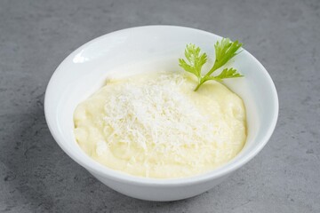 Creamy mashed potatoes topped with grated cheese and garnished with fresh parsley, served in a white bowl on a gray background