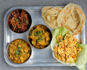 Traditional Indian meal with paratha bread, spicy chickpea curry, mixed vegetable curry, scrambled paneer, and dry chutney served on a stainless steel tray