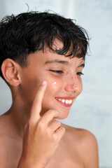 Hormonal changes, skin care, and adolescence. Preteen boy applying a drying gel to an acne pimple.