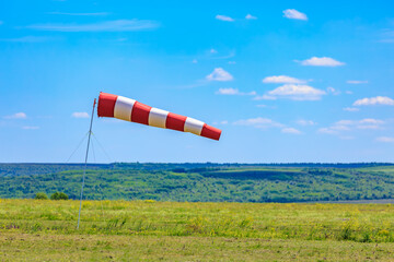 Red and white windsock in open field with clear sky and green landscape