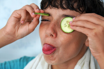 skin care and adolescence. Teenage boy with slices of cucumber on his eyes sticking out his tongue.