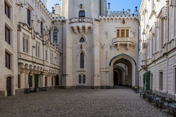 Gothic castle courtyard with stone facades and arched entrance, blue sky