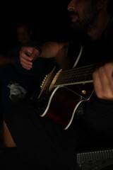 Man playing acoustic guitar at night, close-up of hand strumming strings