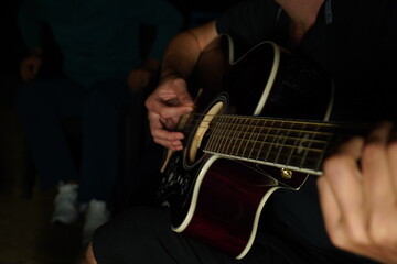 Man playing acoustic guitar at night, close-up of hand strumming strings