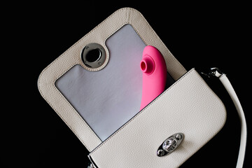 Pink vibrator, partially visible from white handbag, on dark blurred background.