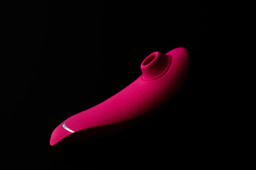 Close up of pink sex toy stimulator with water drops, placed against a blurred black background
