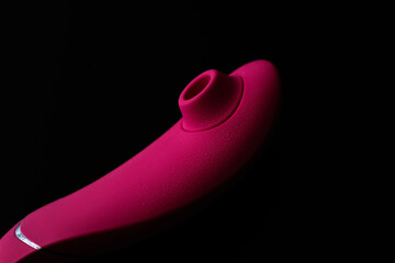 Close up of pink sex toy stimulator with water drops, placed against a blurred black background
