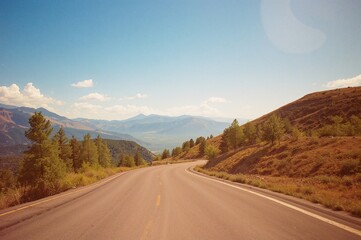 Fototapeta premium Curvy mountain pathway under a clear summer sky with trees and scenic views