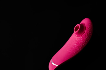Close up of pink sex toy stimulator with water drops, placed against a blurred black background