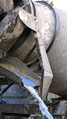 Water flows down the chute of a concrete mixer. Washes the concrete mixer after use. Washing away the remaining cement mixture. Cleaning of special vehicles. Dirty water. Construction site. Vertical.