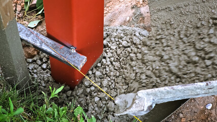 A builder pours a wet concrete from a mixer truck into a foundation. Pouring cement into pit with pillar. Foundational work. Workers control a mix flows through the gutter. Building industry.