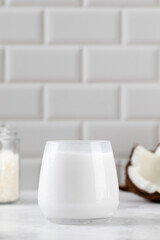 Fresh coconut milk in glass with sliced coconut and white tile background. Alternative milk