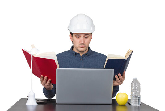 Stressed young man engineer wearing white helmet, sitting at the working desk looks confused in his laptop as holds books in both hands, isolated on transparent background
