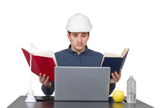 Stressed young man engineer wearing white helmet, sitting at the working desk looks confused in his laptop as holds books in both hands, isolated on transparent background - Powered by Adobe