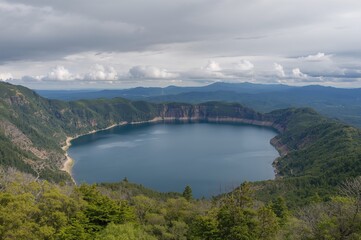 Experience a breathtaking panorama of the vast caldera lake and the scenic mountain pass from the summit of the observation path during a late summer morning in the northeastern region.