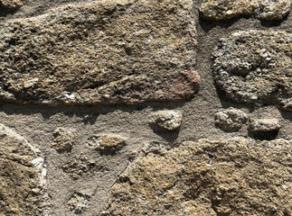 Close-up view of an old stone wall surface showing rough texture, uneven shapes, and natural earthy