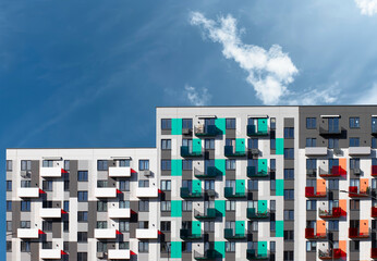 Modern apartment building with colorful balconies in teal, white, and red under a bright blue sky