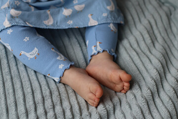 Close-up of baby feet in blue pajamas with white patterns, resting on a soft gray textured blanket.