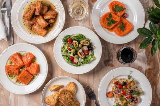 Top view of a festive dinner table featuring an assortment of appetizers and salads including salmon, olives, wine, vegetables, grilled fish, and toast. A family holiday meal setting for occasions