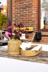 Ceramic vase with purple flowers and wooden cutlery tray on rustic outdoor table in daylight.