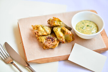 baked zucchini flowers in a white plate on a cutting board with sauce on a white background