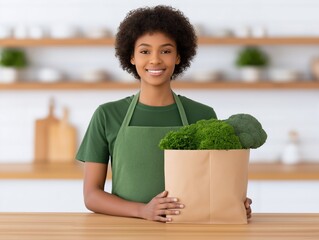African American woman wearing green apron is smiling while holding a paper bag filled with fresh green vegetables in a bright kitchen setting, showcasing healthy lifestyle choices