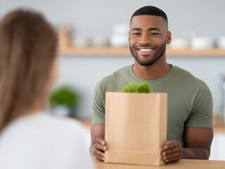 Smiling African American man presenting a paper bag with fresh greens to a woman in a bright kitchen, showcasing healthy food delivery and friendly interaction