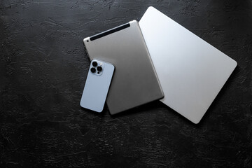 Obraz na płótnie Canvas Silver laptop with tablet and mobile phone - high tech gadgets on black stone background, top view