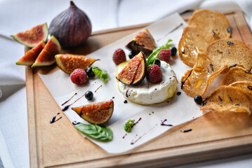 figs drizzled with balsamic sauce on a wooden board with camembert cheese and bruschetta macro photo