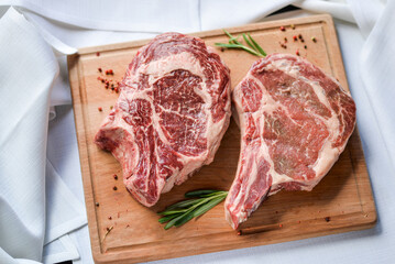 two huge raw steaks of meat on a wooden board