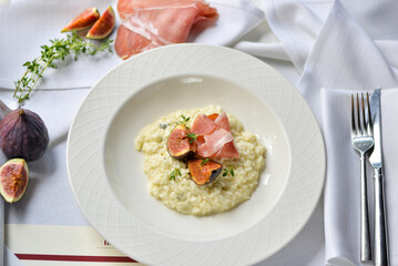 risotto with figs and ham in a white plate on the table