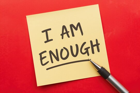 Sticky note on vibrant red backdrop with handwritten message 'I AM ENOUGH', uplifting affirmation for self-love and acceptance, recognizing your value and worthiness, embracing imperfections and flaws