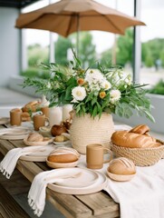  beautifully arranged outdoor dining table featuring fresh flowers, baked goods, and rustic tableware under a shaded umbrella.