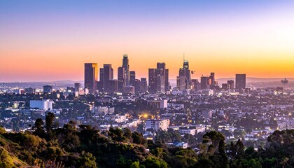 Obraz premium City skyline at sunset. Tall buildings dominate landscape. Hills & trees in foreground. Orange, purple, blue sky