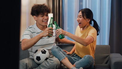 Asian new marriage couple sit on sofa excited cheering watching football sport game on television...