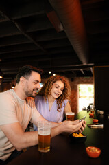 Couple enjoying drinks and looking at smartphone at bar counter