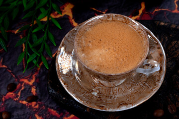 Black coffee with foam in a brown ceramic cup on a dark background