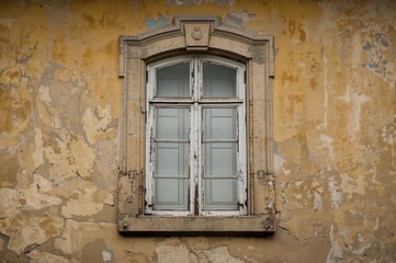 Fototapeta premium Old yellow stone wall featuring a window with a white wooden frame. Classic architectural elements and textured background.