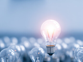 Glowing light bulb standing out among many unlit bulbs, symbolizing innovation and bright ideas in soft blue background