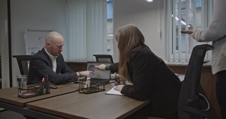 Young professionals collaborate on a project in a modern startup office, analyzing charts and data on a laptop. Teamwork and innovation in business. - Powered by Adobe